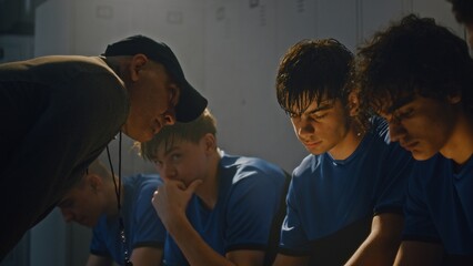Obraz premium Middle Aged Sports Coach Lecturing Youth Soccer Team in Locker Room. Team Sits Quietly on Benches, Processing Harsh Feedback. High Stakes, Tension, and Emotional Weight of Competitive Youth Sports.