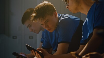 Friendly Interaction in Youth Sports Dressing Room Where Group of Teenage Football Players Using Smartphones and Chatting. One Boy Showing Funny Video or Social Media Content to Teammate. Camaraderie. © Framestock