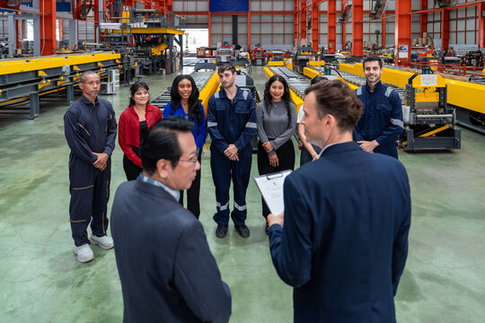 employees and factory staff standing in a row while meeting with two male executive and manager seen from back view during factory tour