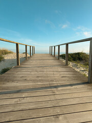 Fototapeta premium Wooden walkway leading to the Atlantic Ocean in Furadouro, Ovar, Portugal, surrounded by sandy dunes under a clear blue sky on a summer day