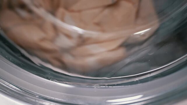 A close-up view showing wet garments tumbling in soapy water during an active wash cycle. Concept of daily domestic chores, cleaning routines, and authentic household lifestyle.