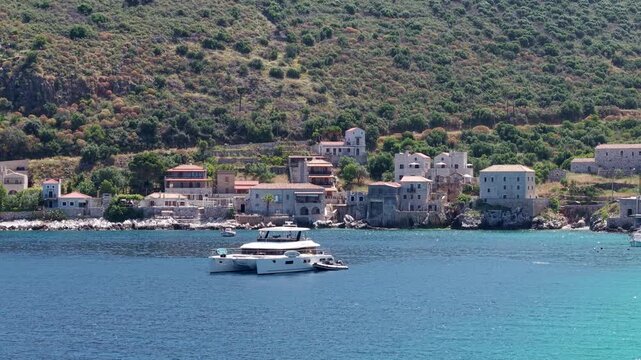 Sunny day yachting in the crystalline turquoise waters, Limeni village on Mani Peninsula with steep lush mountains, seaside stone tower houses in the backdrop, Aerial view