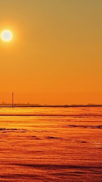 Winter sunset over snow covered fields beneath glowing orange sky, vertical backdrop, drone orbit over twinkling landscape