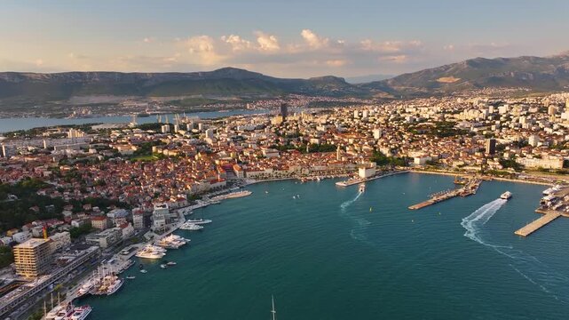 The harbor of Split, Croatia features boats and yachts. Surrounding buildings are visible on the waterfront. Mountains are in the background. Daylight illuminates the area.
