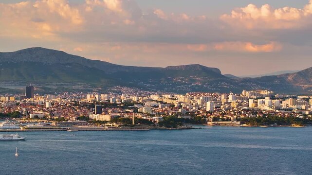 This shows Split Croatia with the coastline and buildings in the distance. The mountains are visible behind the city. The sky has clouds with different colors.