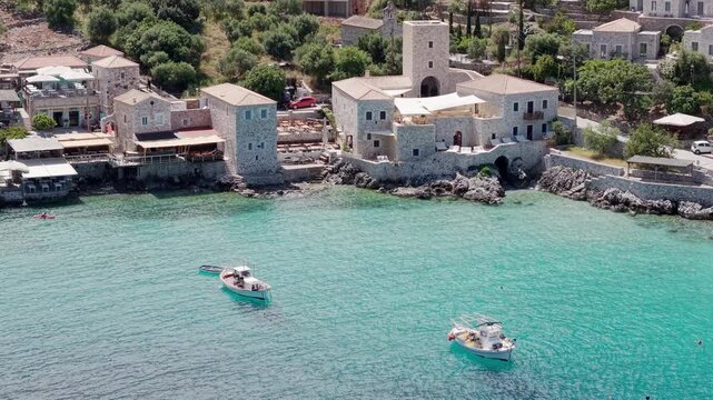 Aerial pullback shot of Limeni village traditional stone tower houses to rocky coastline on turquoise waters on sunny day