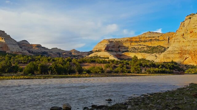Harding Hole backcountry camping overlook spot, golden canyon cliffs rising above the Yampa River with vegetation along the shoreline, alpenglow light on rocks