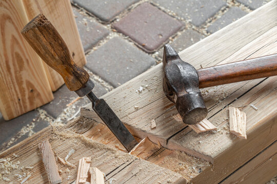 Traditional woodworking tools on a timber beam in a carpentry workshop. Vintage wood chisels and a hammer resting on processed lumber surrounded by wood shavings. Concept of craftsmanship, carpentry, 
