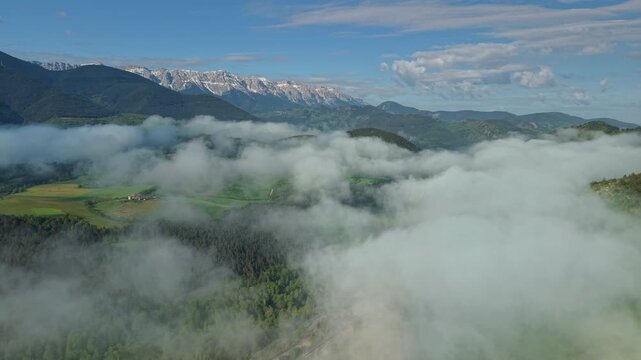 Snow capped Pyrenees mountains above fog covered forests and green countryside in Catalonia