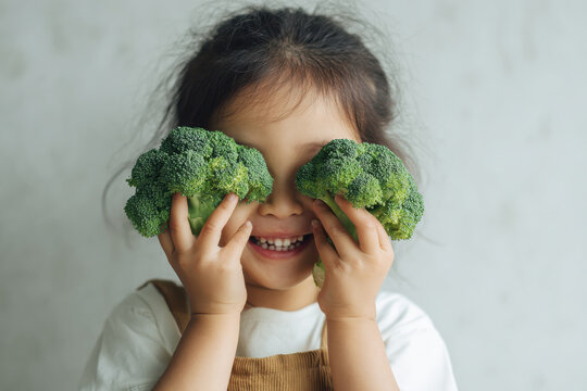 Happy child holding broccoli and smiling while playing with fresh vegetables in a healthy lifestyle concept