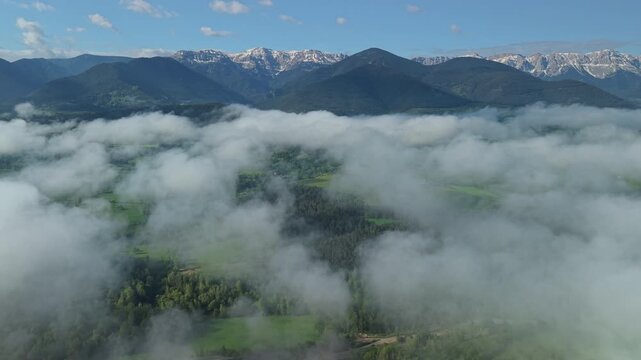 Snow capped mountain range above drifting clouds and green valley in Catalonia