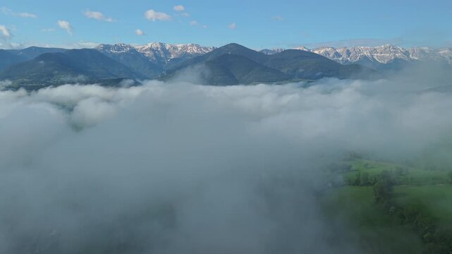 Mountain range rising above sea of clouds over green valley in Catalonia