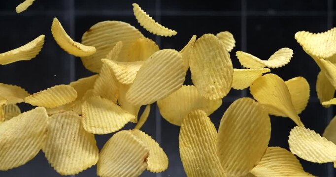 Ridged potato chips falling in slow motion on black background