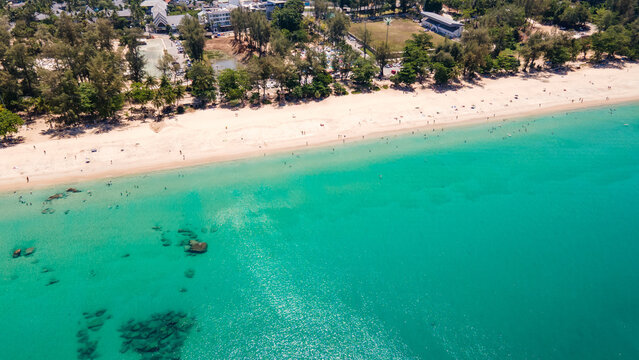 Aerial top view of Surin beach in Phuket, Thailand. Turquoise waves reach the Andaman sea coastline while tourists relaxing on the beach. Travel attraction for summer vacation