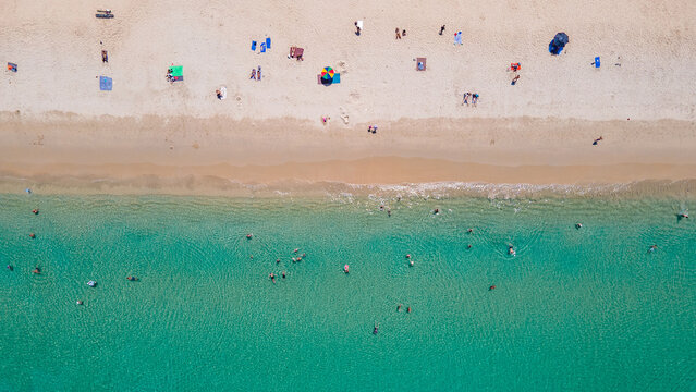 Aerial top view of summer activities on tropical beach landscape at Surin beach in Phuket, Thailand. Turquoise waves reach the coast while tourists sunbathing, swimming and relaxing on vacation travel