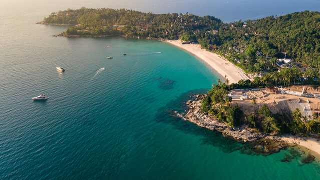 Aerial top view of Pansea Beach in Phuket, Thailand. Turquoise waves reach the Andaman sea coastline with tour boats speeding during sunset. Travel attractions for summer vacation in southeast asia