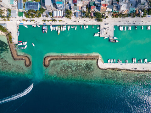 Aerial top view of seaside hotels and jetty with tour boats parking inside the breakwaters at Maafushi island. Travel industry in Kaafu Atoll, Maldives