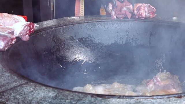 Fresh beef is carefully added to hot vegetable oil in a large traditional cast iron kazan to begin cooking authentic Central Asian pilaf. A key stage of preparing the flavorful zirvak base 