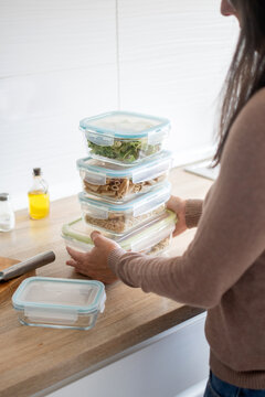 Woman stacking healthy meal prep containers in a home kitchen
