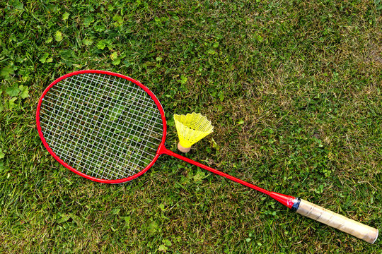 Badminton Racket and Shuttlecock on Grass. Red badminton racket and yellow shuttlecock lie on green grass in an outdoor top view scene.