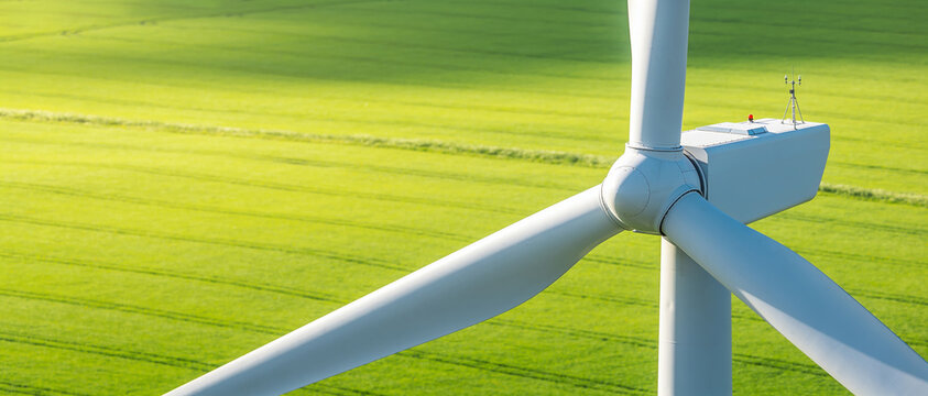 Close-up of a wind turbine nacelle and rotor with an anemometer against bright green fields.