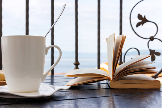 White coffee cup and open book on a balcony table overlooking the Adriatic Sea in Makarska, Croatia. 
