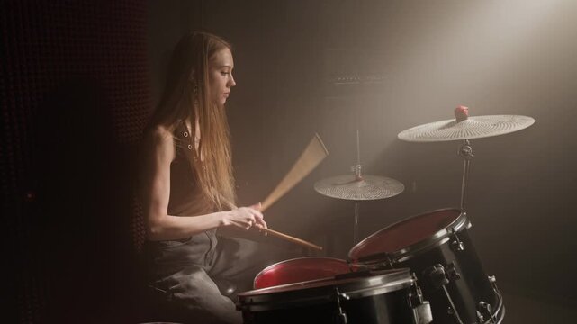 Zoom in shot of young woman playing drums energetically in music studio. Footage for music school advertisements, instrument retail promos, or creative hobby campaigns