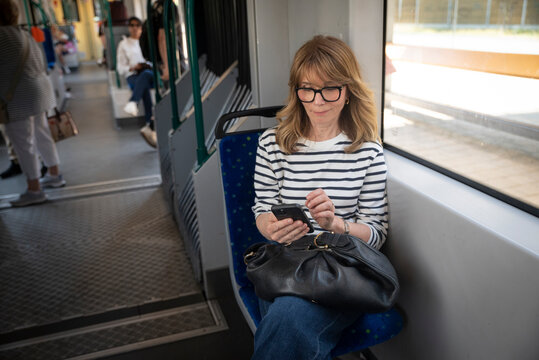 A middle-aged woman riding the tram and using a smarpthone