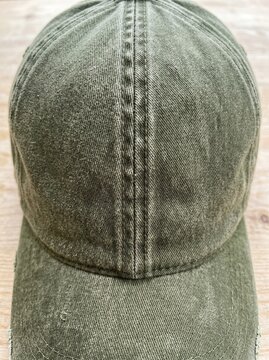 Close up of an olive green washed cotton baseball cap with distressed texture on a light wooden background, casual vintage fashion concept.