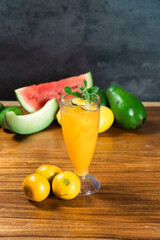 Tropical Refreshment: A vibrant glass of orange juice, adorned with mint, stands as a centerpiece amidst an assortment of fresh fruits like watermelon, avocado, and citrus. © andreas