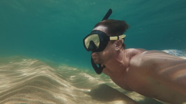 Person dives and swims with mask along the empty sandy sea bottom