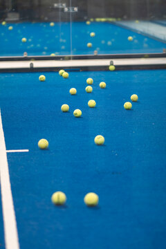 Padel Court Scattered with Balls: A blue padel court dotted with numerous yellow balls, awaiting players for a game. The blue surface and white lines contrast with the scattered balls.