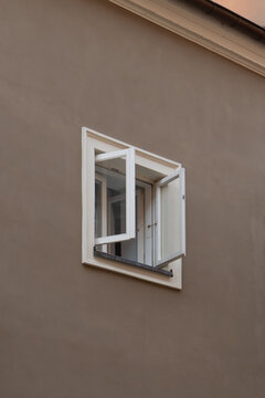 An open window with white frame on a solid brown stucco building facade