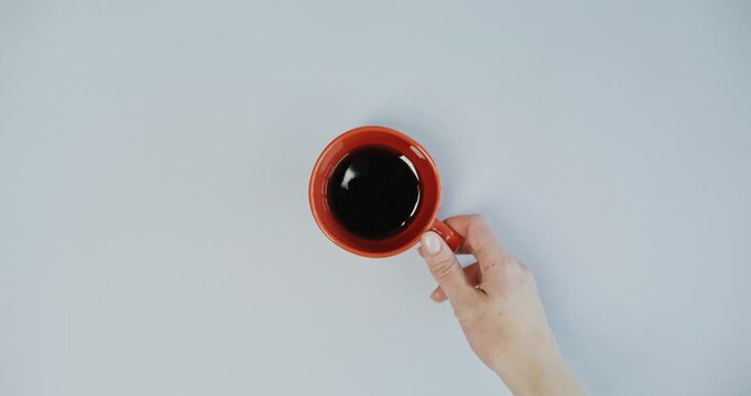 Hand Picking Up Orange Coffee Cup From Minimalist Gray Background
