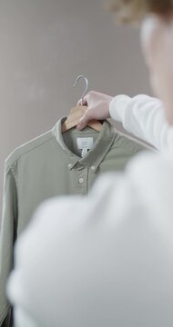 Person holding an olive green button down shirt on wooden hanger