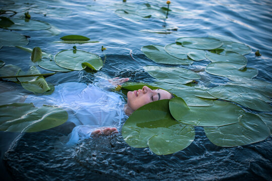 Mystical Slavic water nymph or Mavka floating in a dark river among water lilies, ancient mythology concept with a beautiful woman as a river spirit, pagan folklore and ethno fantasy atmosphere