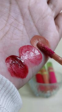 Applying nude or skin tone lip tint to palm using makeup brush. Vertical close up. Natural lip color swatch for cosmetic presentation.