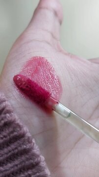 Applying lip tint color on palm skin using brush applicator. Vertical close up view. Lip product swatch for beauty and cosmetic presentation.