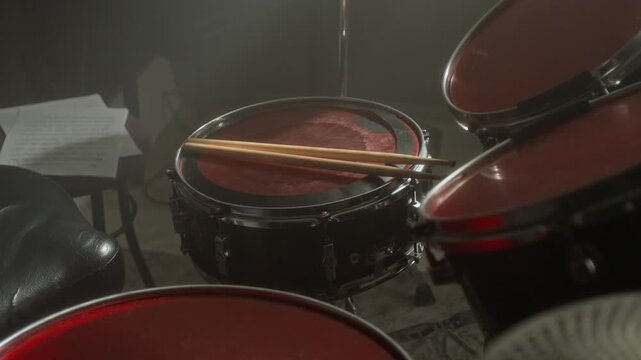Drum kit with red drumheads and wooden drumsticks resting on snare drum in music studio. Clip for music school promos, concert ads, or band trailers