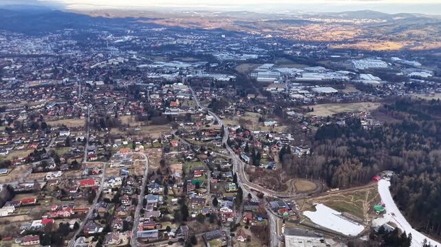 Aerial Sunset Suburb Panorama Showing Rooftops And Winding Roads, Patchy Snow Fields, Distant Mountains, Soft