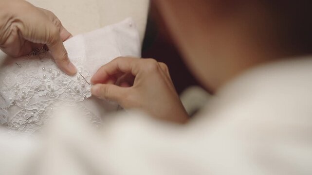 Hand stitching pearl embellished lace onto bridal dress during couture production