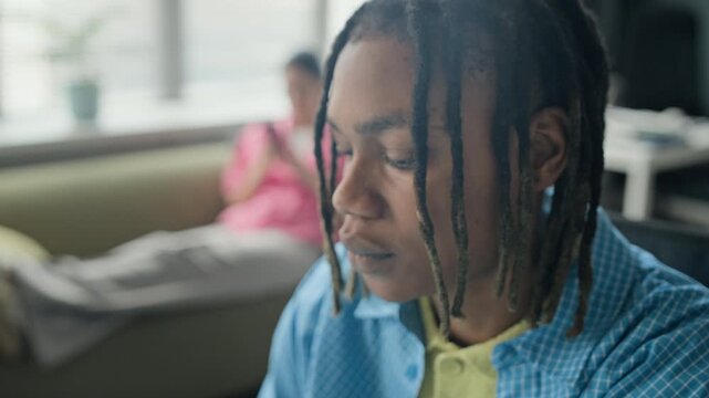 Closeup of African American young adult man putting on headphones and closing eyes to take mindful break in office. Video represents workplace mental health, stress relief, and corporate wellness