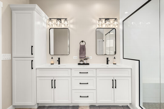 A bathroom with brown walls, white cabinets, black fixtures and hardware, and a walk-in shower with white tiles.