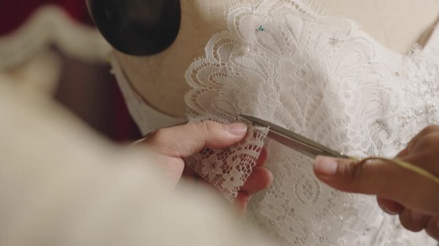 Precision trimming lace edge on custom bridal gown during couture finishing