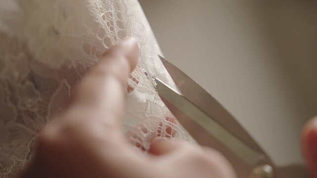 Close up of trimming lace detail on handcrafted bridal gown with precision scissors