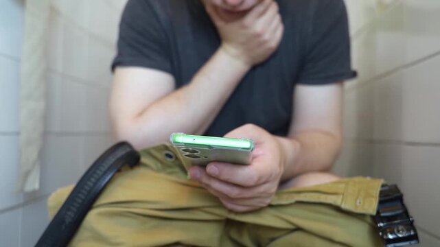 Man sitting on the toilet with a smartphone in hands. Guy scrolling phone on the loo, concept of prolonged sitting risk, screen addiction, and hemorrhoids.