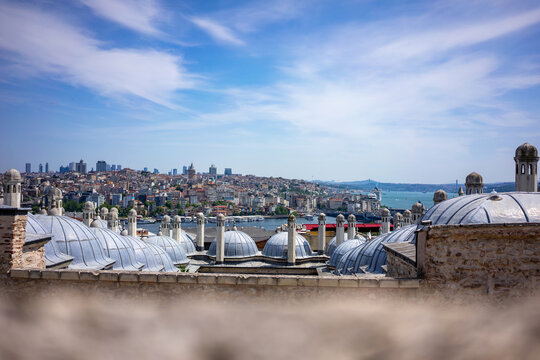 A sweeping panoramic view from above shows Istanbul's cityscape with mosque domes in the foreground, the Golden Horn waterway, and the Galata Tower rising on the distant hillside.