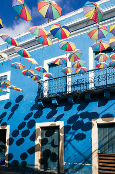 Colorful umbrellas suspended over a street with blue building, Olinda, Pernambuco, Brazil