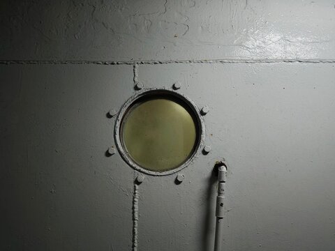 Classic round porthole window with a bolted frame on a heavy white steel bulkhead wall of a ship