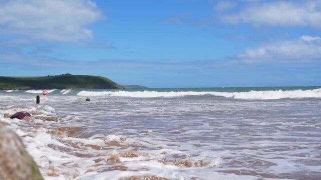 A young man with an athletic build walks along shore of the Atlantic Ocean, swims a little, and sunbathes. The wind and waves urge the guy to get out of the sea